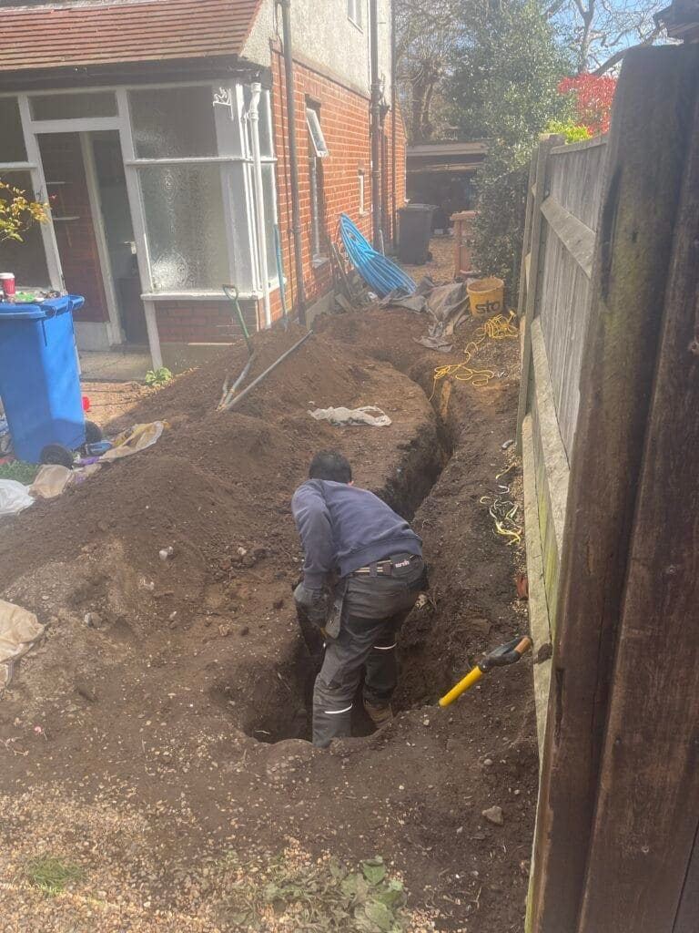 Plumbing engineer carrying out water main installation trench works outside a home in Norfolk